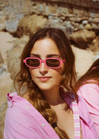 Two women in pink shirts and sunglasses sitting on rocks.