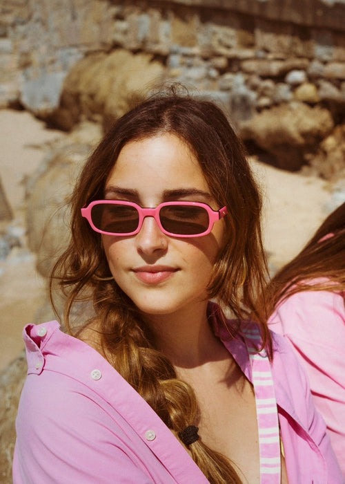 Two women in pink shirts and sunglasses sitting on rocks.