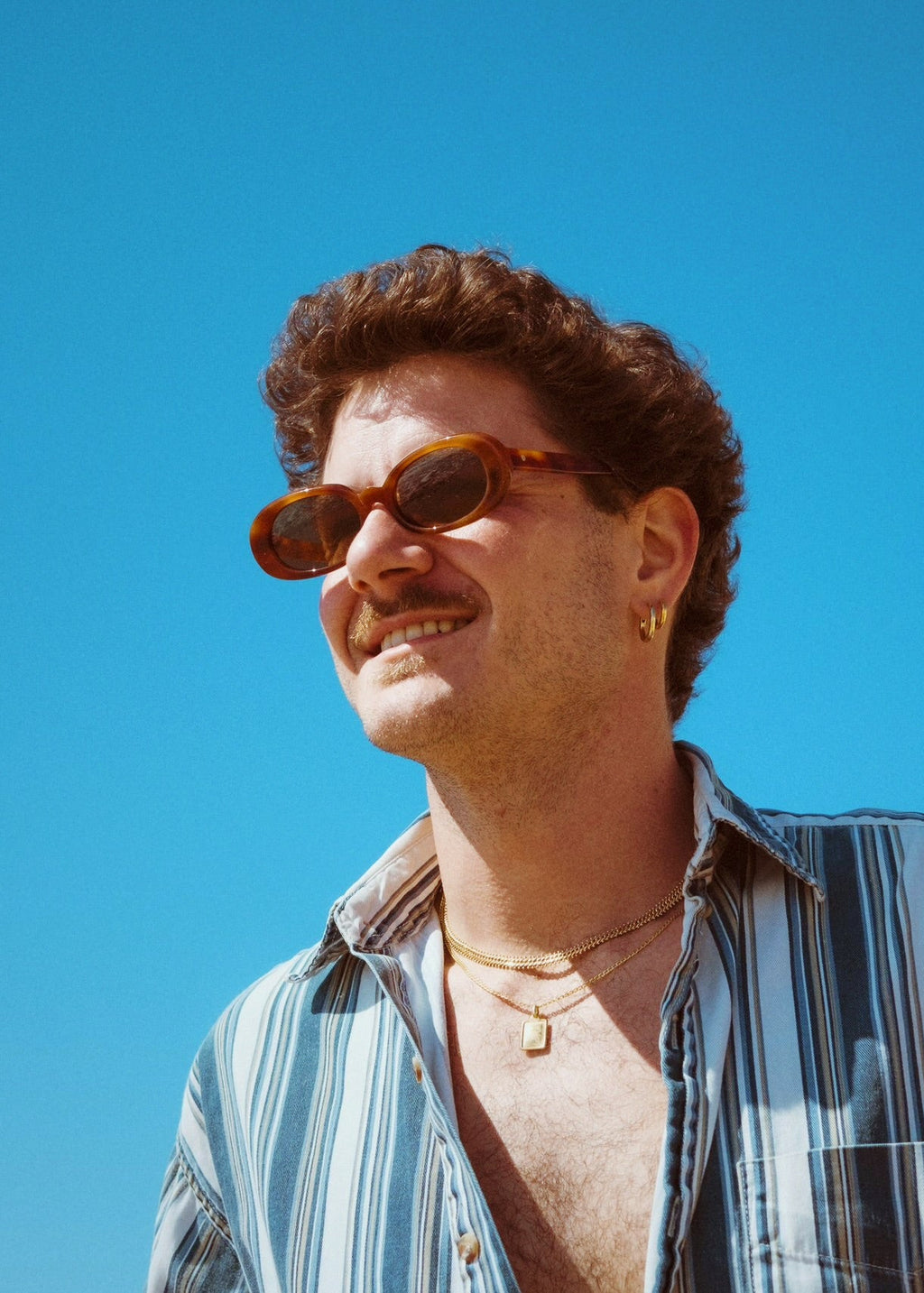 Man wearing sunglasses and a striped shirt against a clear blue sky